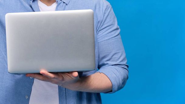 A man in a blue shirt is holding a laptop. Copy space. - Zdjęcie, obraz