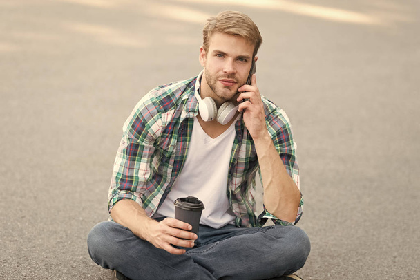 important call. phone call. listen music. ebook concept. man checkered shirt. student relax and recharge. coffee to go. guy drink coffee outdoor. man sit on ground. carefree student in headset - Фото, зображення
