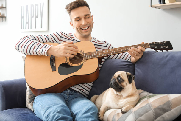 Handsome man with cute pug dog playing guitar at home - Foto, immagini