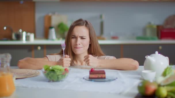 Woman choosing cake instead salad on kitchen. Lady eating cake on kitchen - Filmati, video