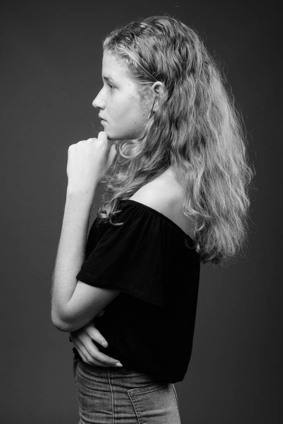 Studio shot of young beautiful blonde teenage girl against gray background in black and white - Foto, afbeelding