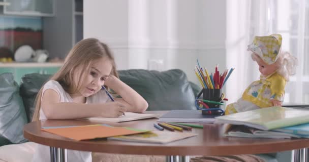 Sad Caucasian schoolgirl doing homework at home. Pretty upset child writing in exercise book and thinking. Intelligence, education, studying. Cinema 4k ProRes HQ. - Materiał filmowy, wideo