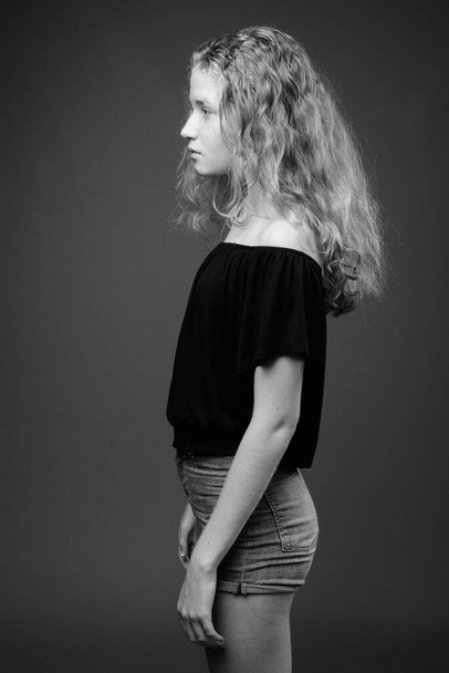 Στούντιο πλάνο του νεαρού όμορφη ξανθιά έφηβη κοπέλα σε γκρι φόντο σε μαύρο και άσπρο - Φωτογραφία, εικόνα