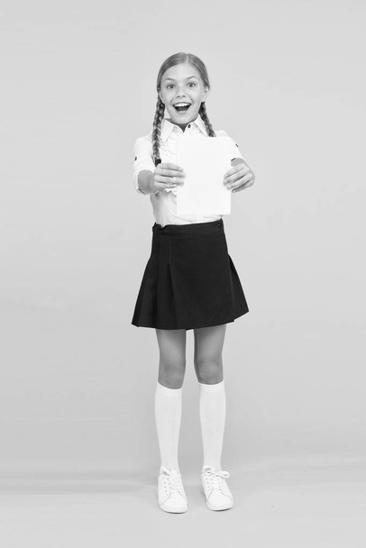 Schoolgirl studying textbook. Exciting literature. Girl child hold book stand yellow background. Kid girl school uniform happy face read book studying. Excited about knowledge. Enjoy studying - Foto, Bild