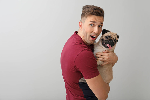 Handsome man with cute pug dog on light background - Фото, зображення