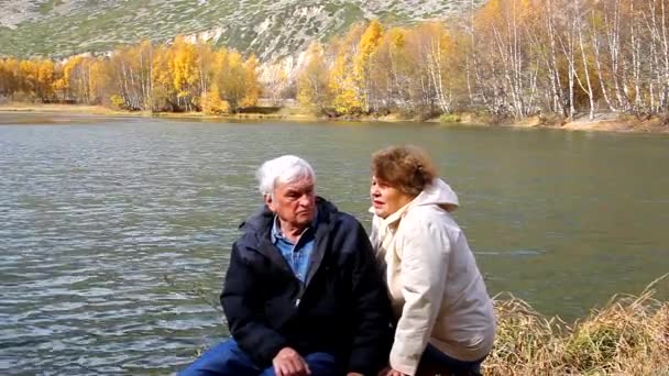 szczęśliwa para podeszłym wieku siedzi i mówi nad jeziorem - Materiał filmowy, wideo