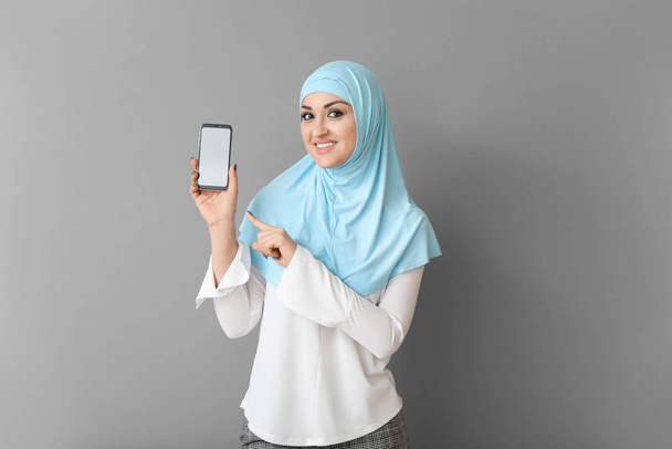 Прекрасна арабська жінка з мобільним телефоном на сірому фоні. - Фото, зображення