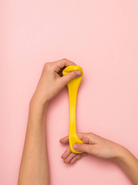 Children's hands stretch a thin bright yellow slime on a pink background. - Photo, Image