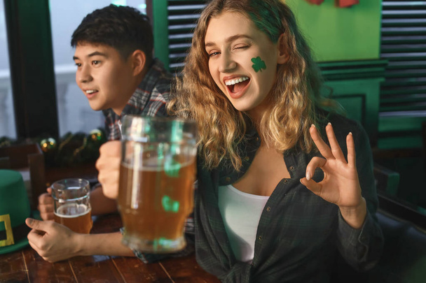 Young woman with friends celebrating St. Patrick's Day in pub - Фото, изображение