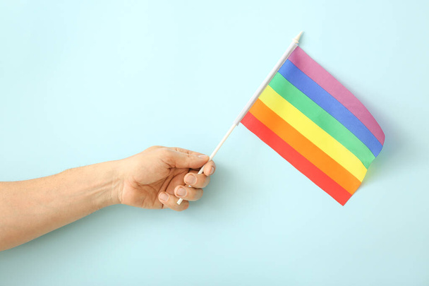 Mano masculina con bandera de arco iris sobre fondo de color. Concepto LGBT
 - Foto, imagen