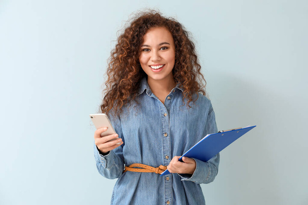 Young African-American businesswoman with mobile phone on color background - Φωτογραφία, εικόνα