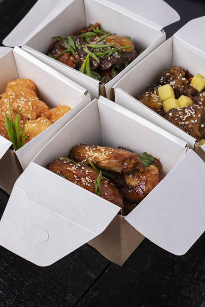 Válogatott kínai ételek papírdobozban: édes és savanyú csirke, tészta, saláta, rizs, párolt zsemle, mártogatós. Lapos fektetés - Fotó, kép