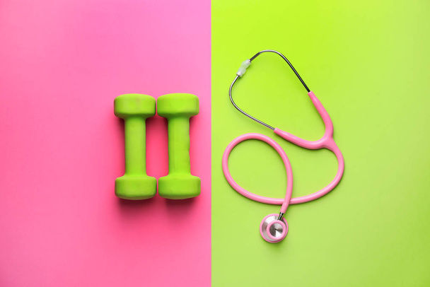 Stethoscope and dumbbells on color background - Photo, Image