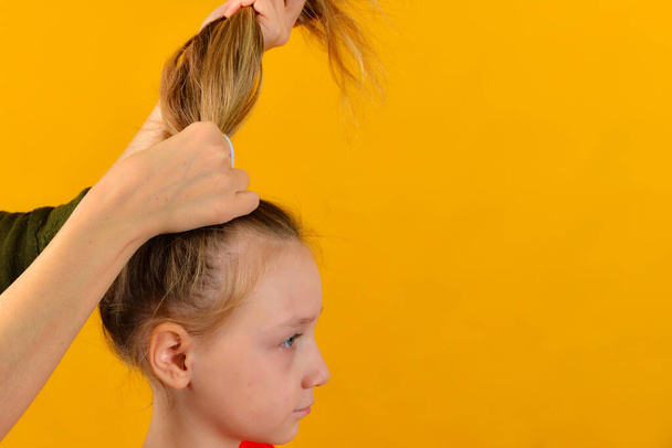 Mom does her daughter's hair by braiding her hair in braids and a tail. - Foto, Bild