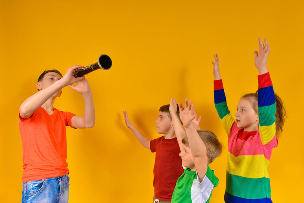 Dětský sbor doprovázený klarinetem. Chlapec hraje na klarinet dětem, a oni zpívají a zvedají ruce. - Fotografie, Obrázek