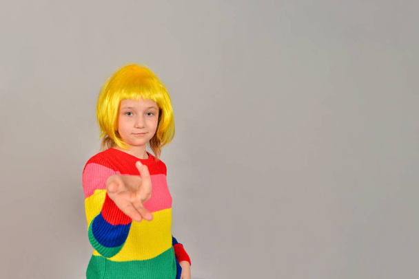 Дівчина в жовтій перуці вказує на місце для рекламного продукту, яскравого кольору дитини на сірому фоні
. - Фото, зображення