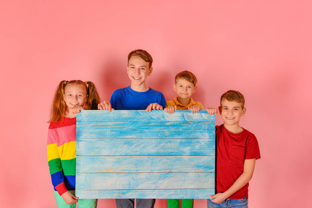 Vier vrolijke kinderen in felgekleurde kleren houden een houten boa vast - Foto, afbeelding