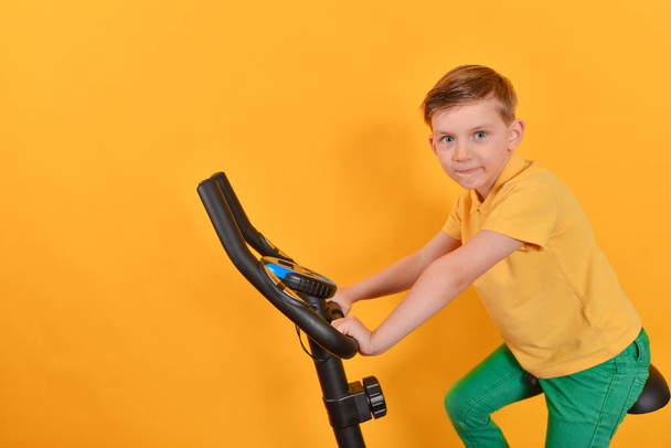 The child goes in for sports on a stationary bike, fitness for children. - Photo, Image