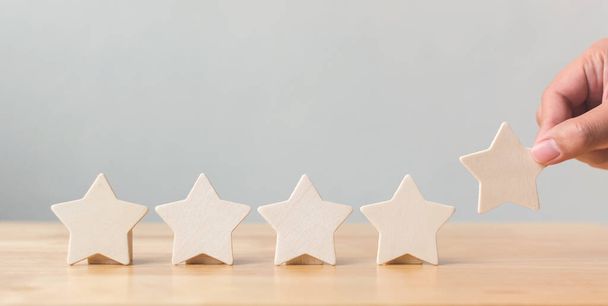テーブルの上に木製の5つ星の形を置く手。最高のビジネスサービス評価顧客体験のコンセプト - 写真・画像