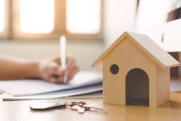 Dřevěný domácí model a klíčový dům na dřevěném stole s ručním podpisem smlouvy o úvěru nebo hypoteční investice do nemovitostí - Fotografie, Obrázek