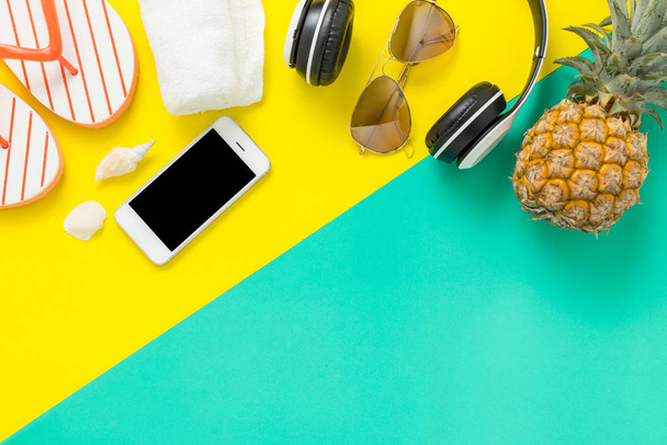 Summer Holidays background Concept, Phone with pineapple, glasses and flip flops On a green and yellow background top view - Foto, imagen