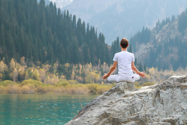 Young zen man in meditation. Outdoor yoga in mountain lake. Exercise Agni Stambhasana. - Photo, Image
