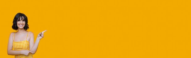 Bella donna caucasica indossa un vestito sta indicando qualcosa con il dito indice e sorridente allegramente su uno spazio vuoto giallo
 - Foto, immagini