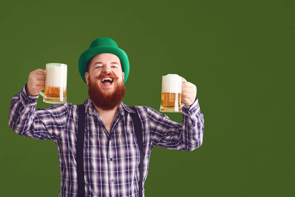 Happy St. Patricks Day. Fat man in a green hat holds his hands up glasses with beer - Photo, image