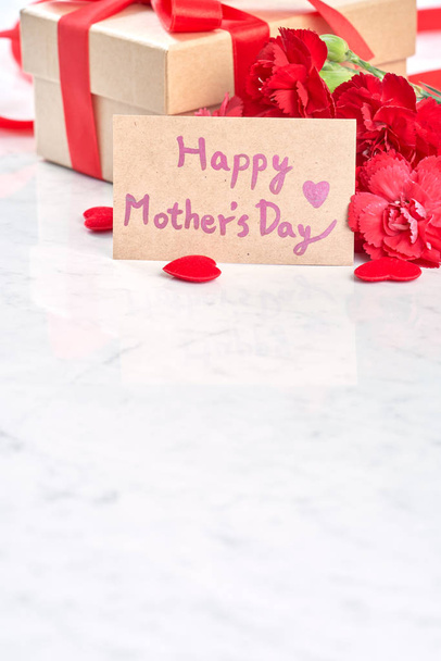 Mother's Day greeting design concept - Beautiful blooming red carnations, gift box with ribbon on white marble table background, close up, copy space. - Photo, image