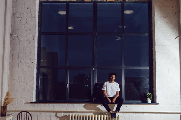 African American man in a white T-shirt sitting on a window. Mock-up. - Fotó, kép