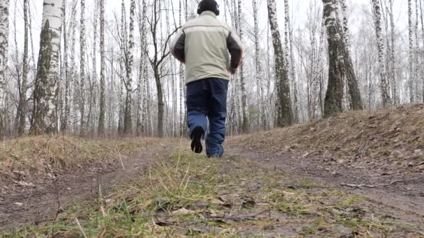 achtergrond een man loopt langs een bospad is training in het bos buiten buiten uit focus op de voorgrond is een swingende boomtak. herfsttijd voor trainers in het bos Joggen 2020 - Video