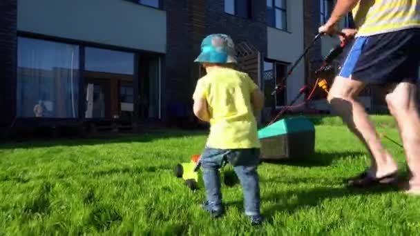 Vater und Sohn der Familie mähen Rasenrasen im privaten Hof. Gimbal-Bewegung - Filmmaterial, Video