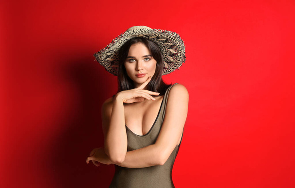 Beautiful woman in stylish swimsuit and hat on red background - Fotoğraf, Görsel