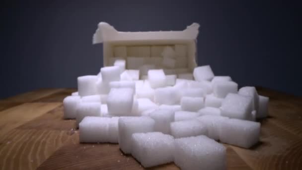 Macro dolly shot of gliding through sugar cubes next into carton box on wooden table. Unhealthy food sweetener, sweet crystal cubes - Felvétel, videó