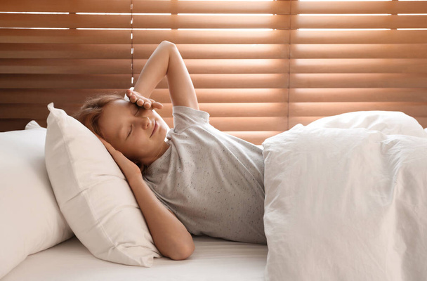 Cute preteen girl awakening in bed near window - Фото, зображення