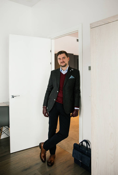 fashionably dressed businessman with a beard - stylish suit, brown shoes, tie, gloves, a man posing in an expensive apartment - Zdjęcie, obraz