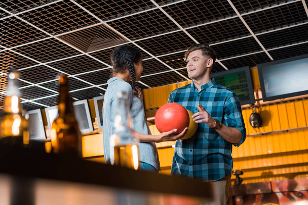 selective focus of smiling man talking to african american girl while holding bowling balls - Valokuva, kuva