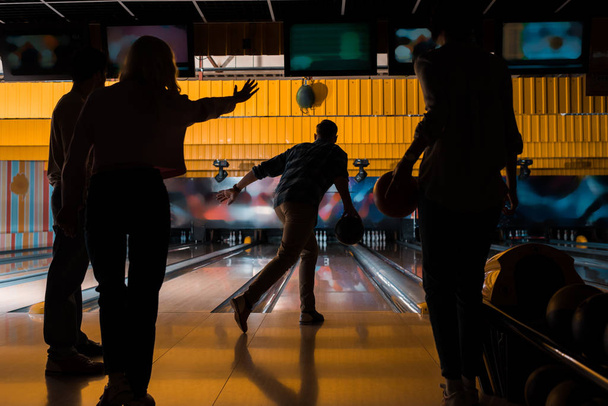 donkere silhouetten van vier vrienden die bowlen in bowlingclub - Foto, afbeelding