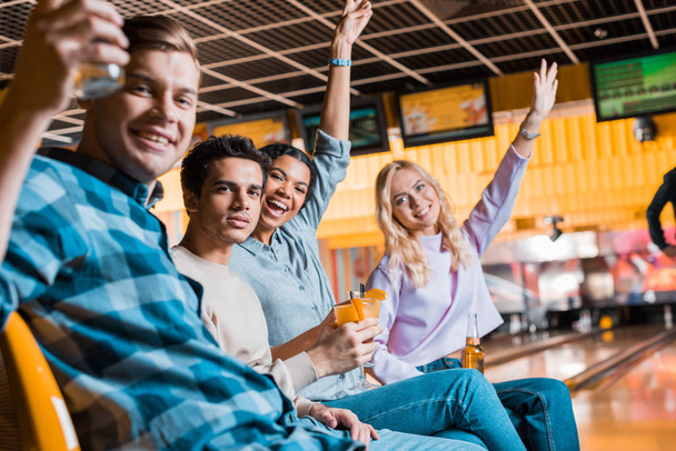 amigos multiculturais felizes sorrindo para a câmera enquanto sentado no clube de boliche com coquetéis e cerveja
 - Foto, Imagem