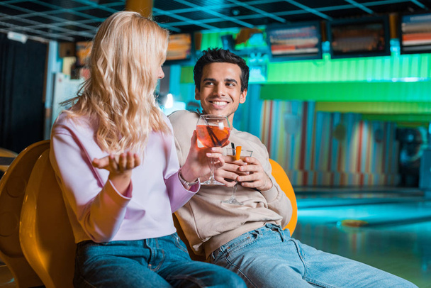 cheerful couple talking while sitting in bowling club and drinking cocktails - Photo, Image