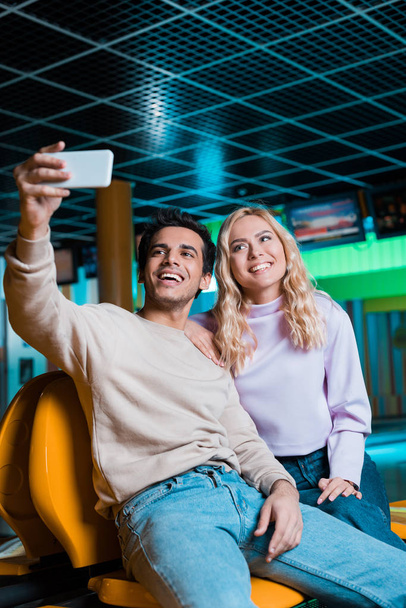 cheerful couple taking selfie on smartphone while sitting in bowling club - Foto, afbeelding