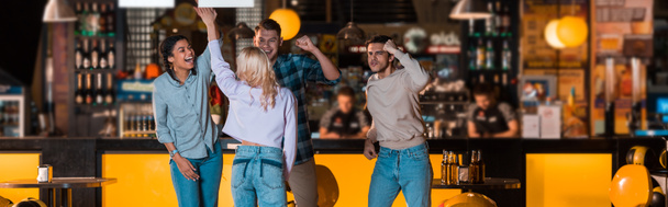 панорамный снимок счастливых мультикультурных друзей, показывающих жест победителя в боулинг-клубе
 - Фото, изображение