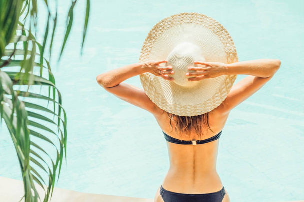 Вид сзади на женщину в купальнике и шляпе возле бассейна - Фото, изображение