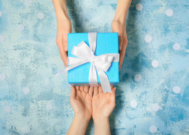 Жіночі руки з красивою подарунковою коробкою на кольоровому фоні
 - Фото, зображення