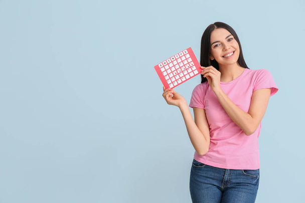Young woman with menstrual calendar on color background - Foto, Imagen