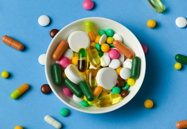 Egy tál tele tabletták, tabletták, vitaminok, gyógyszerek, omega 3 halolaj, gél kapszula, gyógyszer és étrend-kiegészítő egészségügyi ellátás. Kék háttér. - Fotó, kép