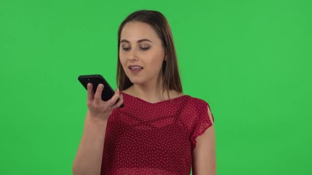 Portrait of tender girl in red dress is asking for information on the network via phone. Green screen - Footage, Video