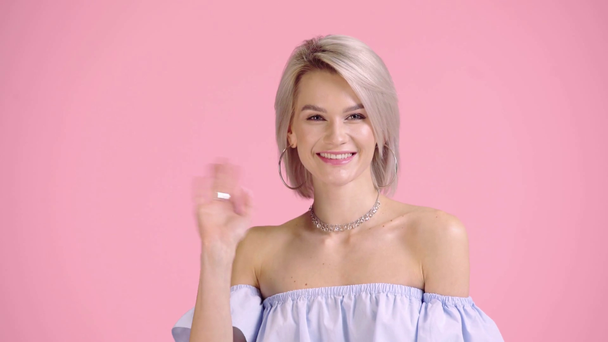 glückliches Mädchen in Bluse mit nackten Schultern winkt Hand isoliert auf rosa - Filmmaterial, Video
