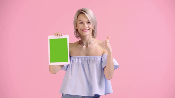 ξανθό κορίτσι δείχνει ψηφιακή ταμπλέτα και δείχνει τον αντίχειρα επάνω απομονωμένο σε ροζ - Πλάνα, βίντεο