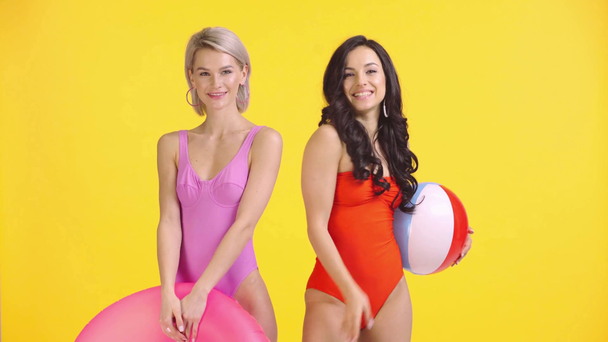 glimlachende meisjes in zwempakken zwaaiende handen, het verzenden van lucht kussen geïsoleerd op geel - Video